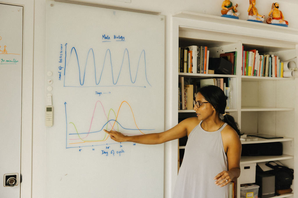 Divya teaching the difference between male and female hormonal cycles on a whiteboard
